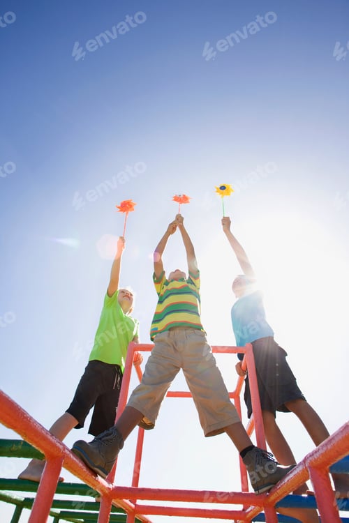 Preview: Boys Holding Pinwheels High Up In The Air Standing On Monkey Bars At A Playground
