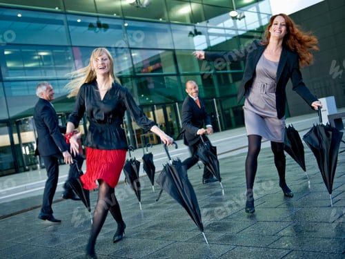 Preview: Four Businesspeople Dancing Outside A Modern Office Building With Umbrellas