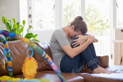 Preview: Unhappy Mother Suffering With Post Natal Depression Sits On Sofa