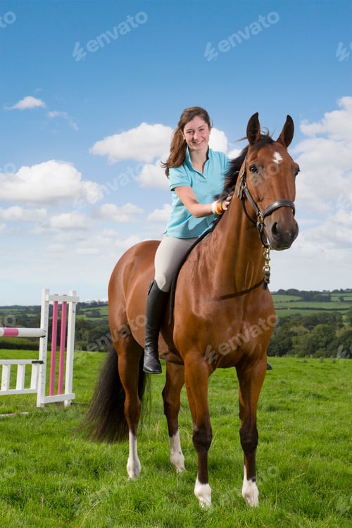 Preview: Vertical Shot Of A Girl Smiling At The Camera While Sitting On A Horseback In A Green Field.