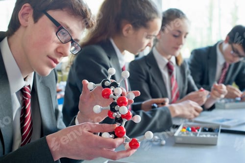 Preview: High School Student Examining A Molecule Model In A Science Class With Her Classmate Sitting In The