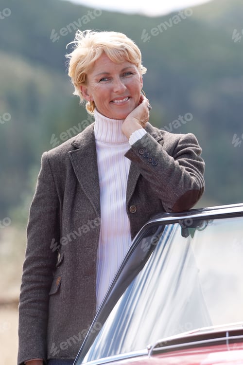 Preview: Portrait Of Mature Woman Standing With Convertible Car In Countryside