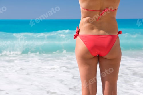 Preview: Back Side Of The Lower Body Of A Woman Standing On A Sunny Beach In A Bikini.