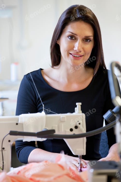 Preview: Vertical Shot Of A Seamstress Smiling At The Camera While Using An Industrial Sewing Machine.