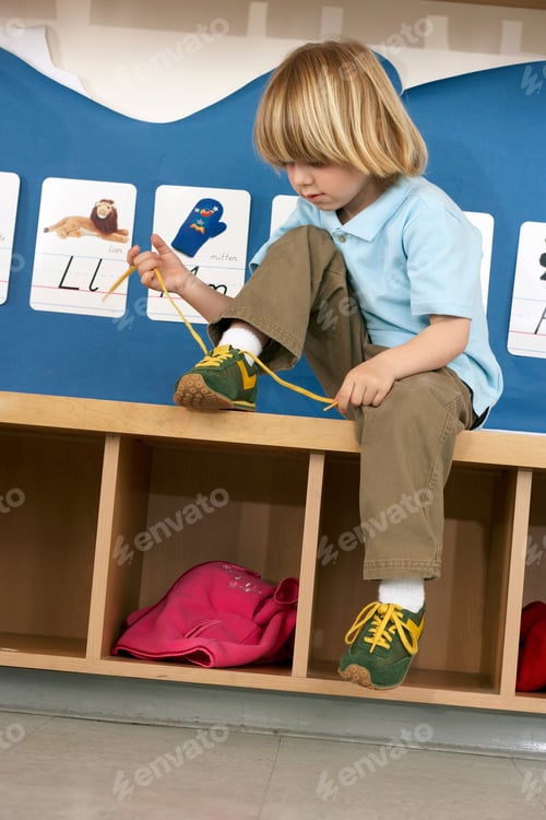 Preview: Vertical Shot Of A Boy Tying His Shoe Lace While Sitting On A Wooden Storage Cabinet In His