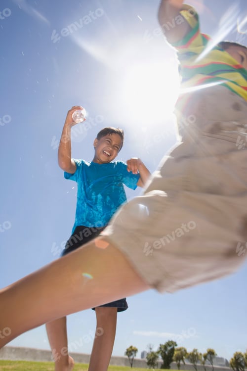 Preview: Vertical Shot Of Boys Squirting Water At Each Other At A Park Using Plastic Bottles