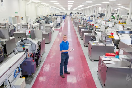 Preview: Wide Shot Of An Engineer Standing In The Aisle Of A Manufacturing Plant With A Clipboard And