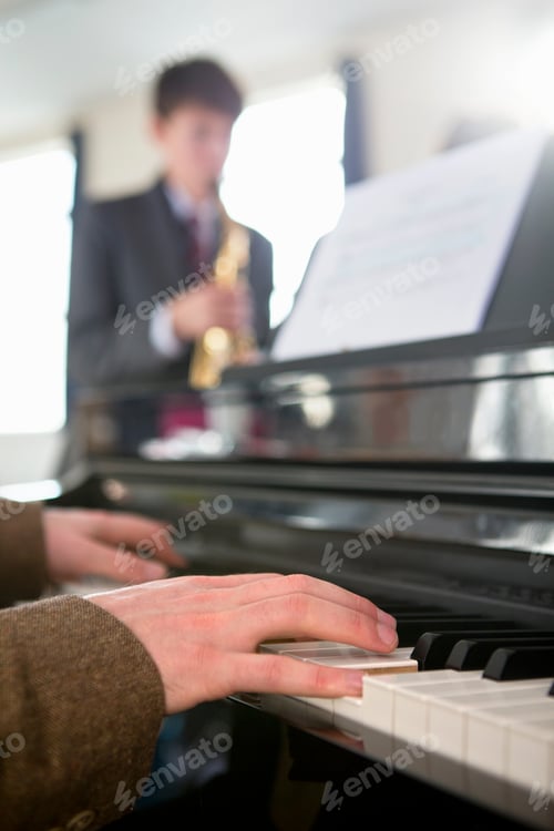 Visualização: Close-up vertical de um professor de música tocando piano com um estudante do ensino médio tocando saxofone