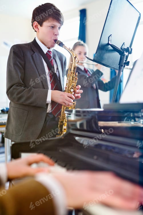 Visualização: Foto vertical de um estudante do ensino médio lendo partituras e tocando saxofone com uma música