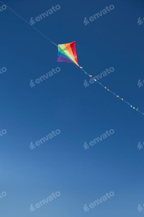 Preview: Vertical Shot Of A Multicolored Kite Flying Over A Blue Sky.