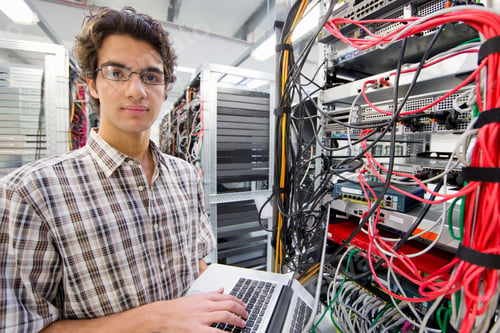 Preview: Technician Looking At The Camera While Working On A Laptop In A Server Room At A Data Center.
