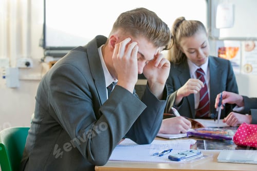 Preview: High School Boy Sitting With His Hands On The Head While Completing His Math Homework.