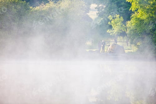 Preview: A Fisherman Standing Beside His Tent At A Distance In Front Of A Misty Lake
