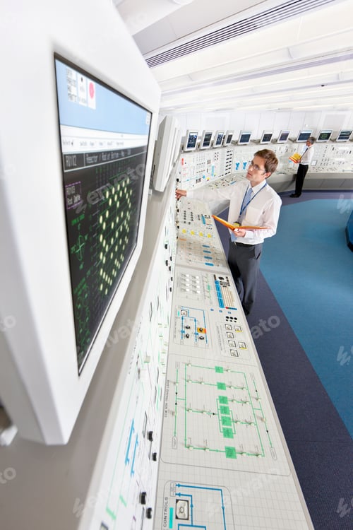 Preview: High-Angle Shot Of A Young Engineer With A File Adjusting Controls While Looking At A Computer