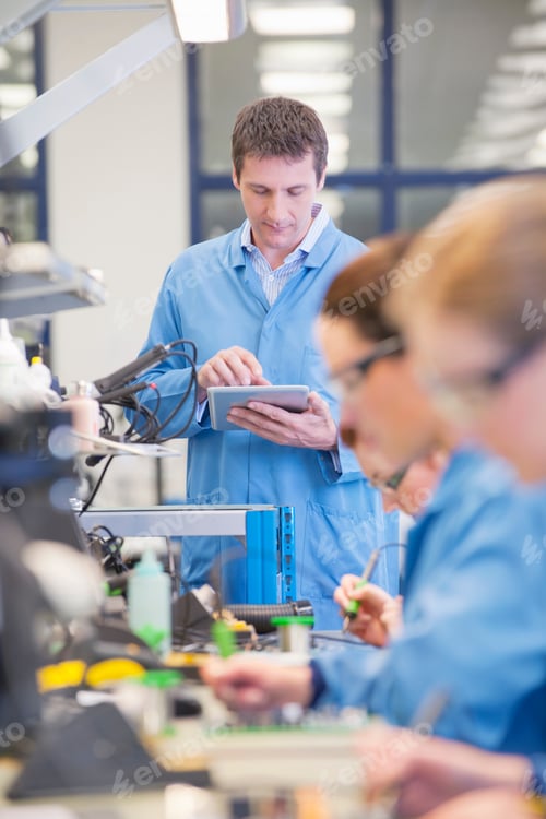 Preview: Vertical Shot Of Supervisor Using A Digital Tablet While Watching Technicians Solder Circuit Boards