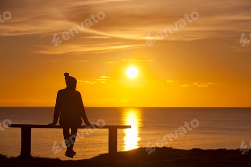 Preview: Silhouette Of A Girl Sitting On A Bench Against The Sunset Over The Ocean.