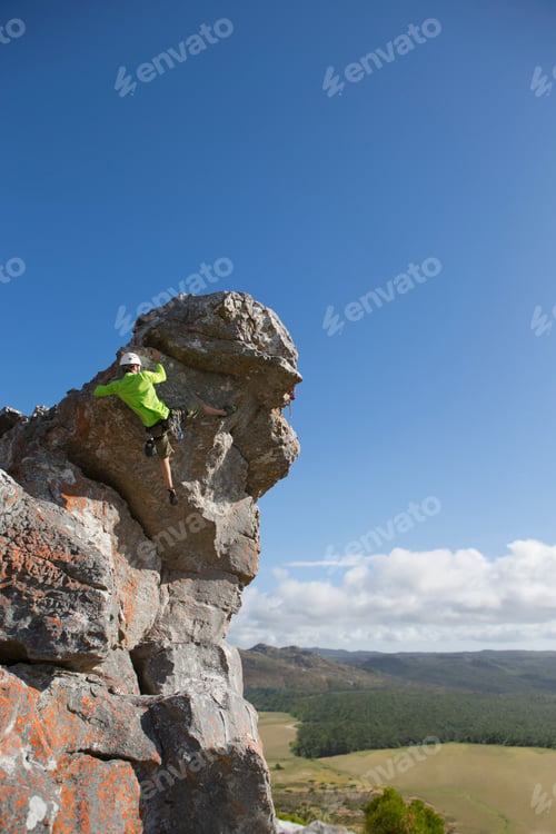Preview: Vertical Wide Shot Of A Male Rock Climber In A Helmet Ascending A Rock Face.