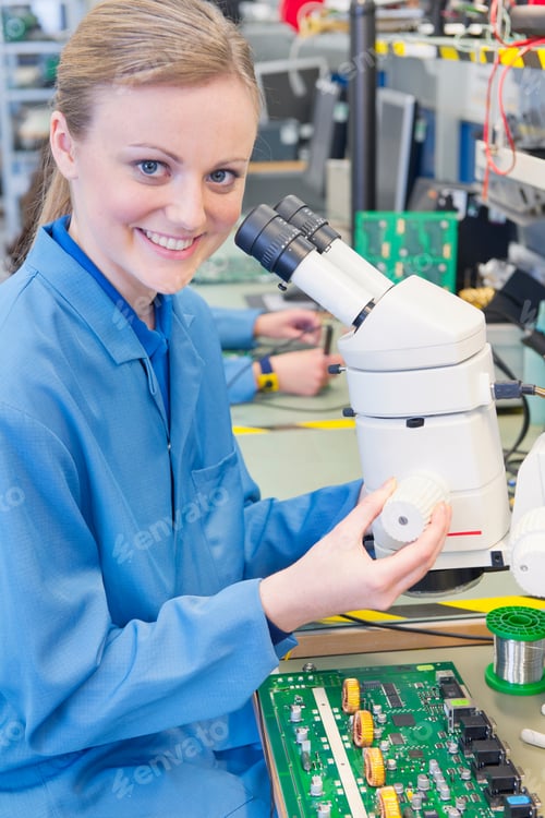 Preview: Portrait Shot Of A Female Technician In An Apron Smiling At The Camera While Using A Microscope To
