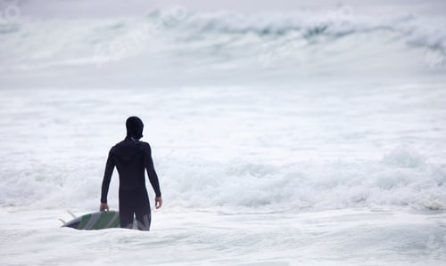 Preview: Man With A Surfboard Standing In The Water At The Sea And Looking At The Waves.