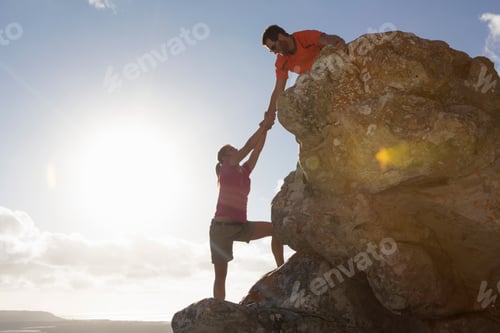 Preview: Wide Shot Of A Male Rock Climber Helping A Woman Climb A Rock Face.