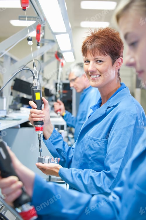 Preview: Vertical Shot Of A Female Technician In Apron Smiling At The Camera While Using An Electric
