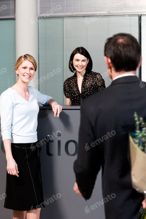 Preview: Businessman With Bouquet Of Flowers Being Greeted By Two Women At Office Reception