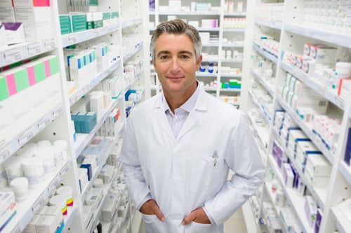 Preview: Pharmacist Smiling With Hands In Pockets In Pharmacy