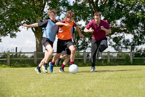 Preview: Middle Schoolboys And Teacher Running While Playing Soccer On The Field In Physical Education
