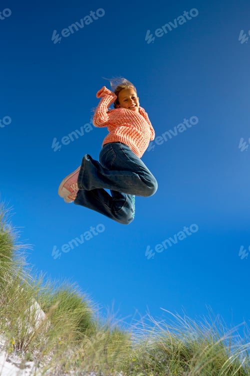 Preview: Exuberant Girl Jumping For Joy Over Sand Dune Beach Grass