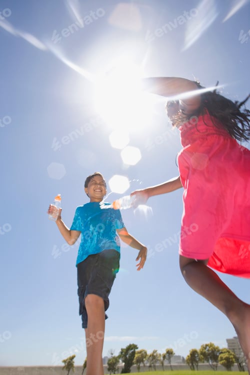 Preview: A Girl Squirting Water At Her Friend At A Park Using Plastic Bottles