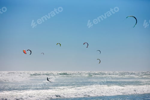 Vorschau: Weitwinkelaufnahme mehrerer Kitesurfer, die über die Meeresoberfläche reiten.