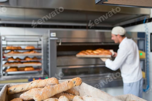 Preview: Close Up Of Breads Kept In A Basket And The Baker Holding A Tray Of Freshly Baked Breads In The
