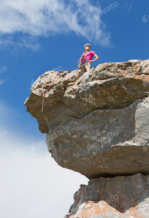 Preview: Low-Angle Vertical Shot Of A Female Rock Climber Standing On Top Of A Rock With Hands In Her Hips.