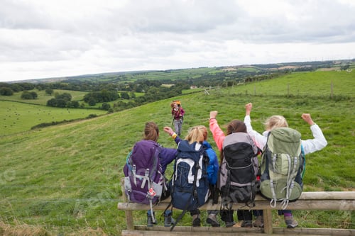 Preview: High-Angle Shot Of The Backside Of A Group Of Girls With Backpacks Sitting On A Fence With Arms
