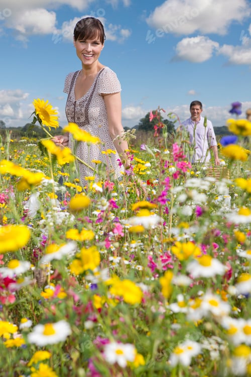 Preview: Vertical Shot Of A Woman Smiling At The Camera With A Man Walking In The Background In A Meadow