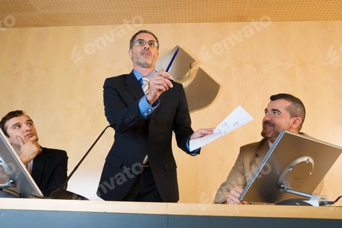 Preview: Three Quarter View Of Businessman Talking In Conference Room And Gesturing At A Document With