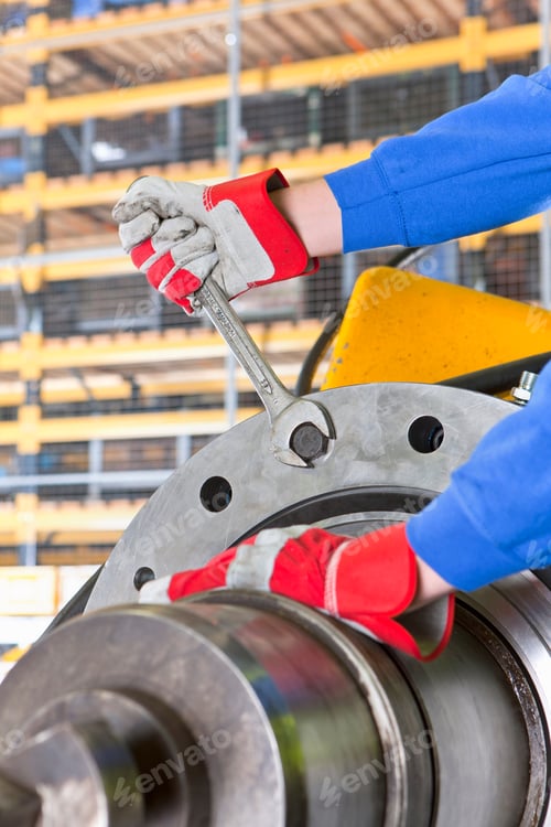 Preview: Close-Up Vertical Shot Of An Engineer With Gloves Tightening Bolts On A Gearbox Casing At A Factory.