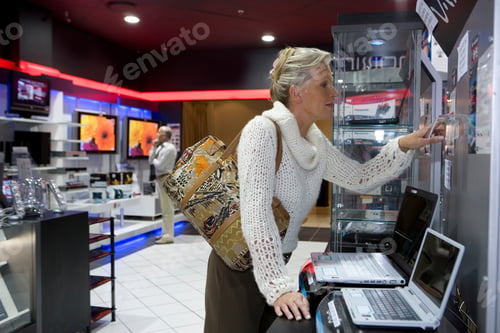Preview: Mature Woman Shopping In Electrical Store For Laptop Computer