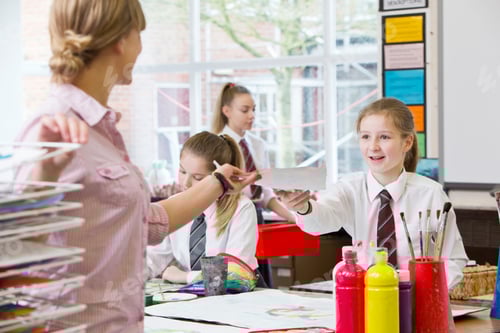 Visualização: Professor de arte tirando uma pintura de um estudante do ensino médio durante uma aula de arte.