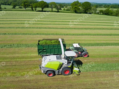 Preview: Aerial View Of Forage Harvester Cutting Grass Silage Crop In Field And Filling Tractor Trailer