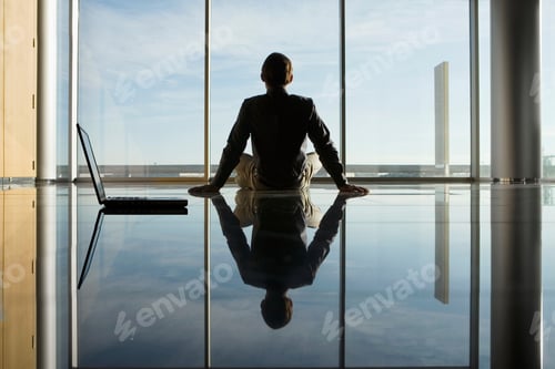 Preview: Reflection Of Businessman Sitting On Floor With Laptop Looking Out Of The Window As Seen From Rear.