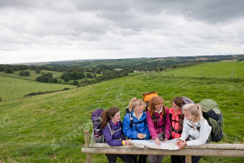 Preview: High-Angle Wide Shot Of A Group Of Girls With Backpacks Looking At A Map And Compass Over A Wooden