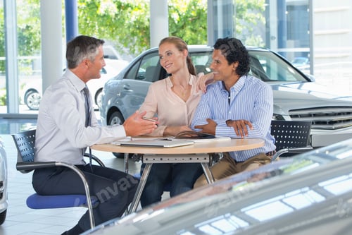 Preview: Salesman Talking To Couple At A Table In A Car Dealership Showroom