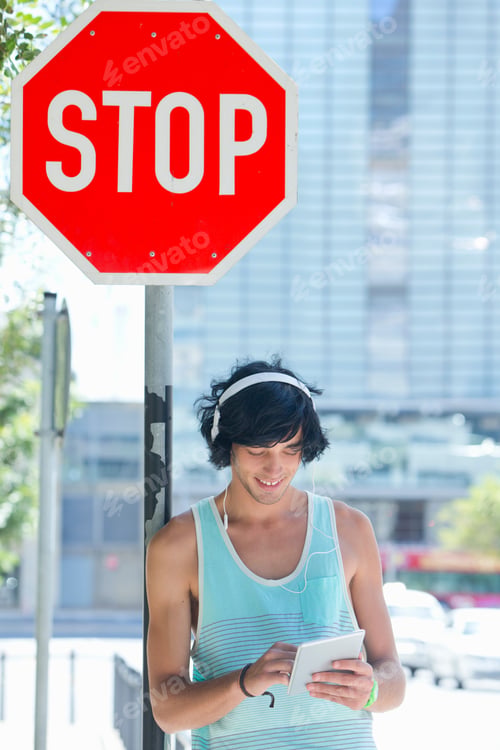 Preview: Smiling Young Man Leaning Against A Stop Sign And Using A Digital Tablet