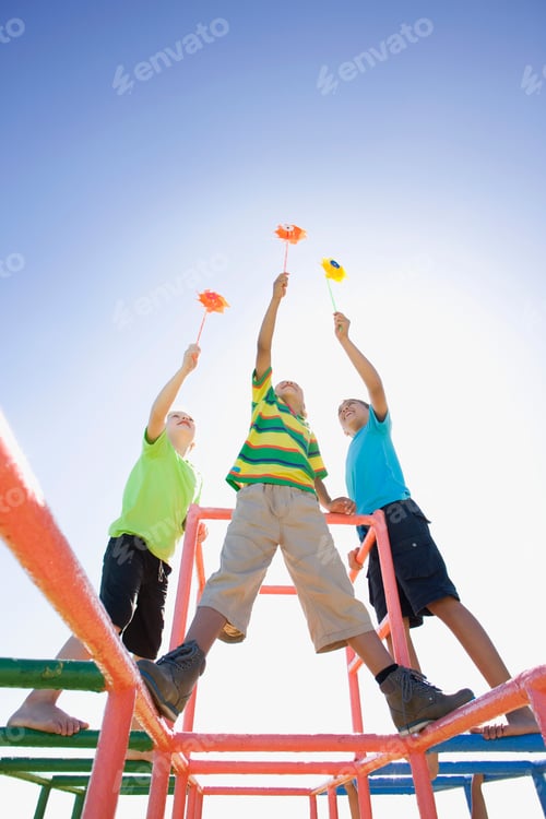Preview: Vertical Shot Of Boys Holding Pinwheels High In The Air Standing On Monkey Bars At A Playground