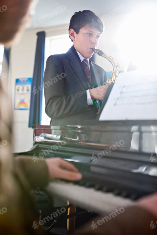 Visualização: Foto vertical de um estudante do ensino médio tocando saxofone com um professor de música tocando piano em