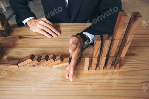 Preview: Close Up Of Businessman Hand Stopping Falling Wooden Dominoes Effect From Continuous Toppled Or