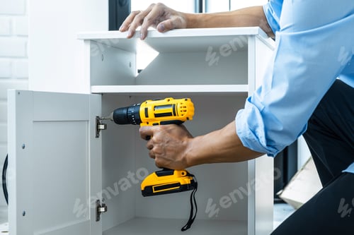 Preview: Man Doing Renovation Work At Home Drilling Wood With Drill Tack On Locker.