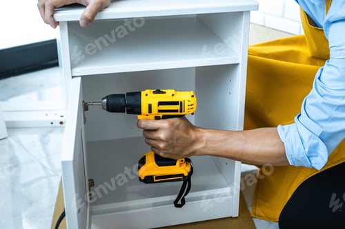 Preview: Man Doing Renovation Work At Home Drilling Wood With Drill Tack On Locker.