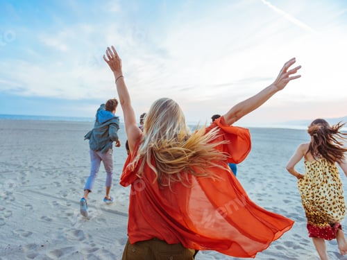 Preview: Group Of Friends Walking Along Beach, Young Woman With Arms In Air, Rear View
